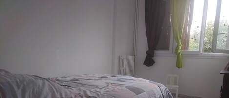 A bedroom with a bed, a radiator, a window with curtains, and a chair.