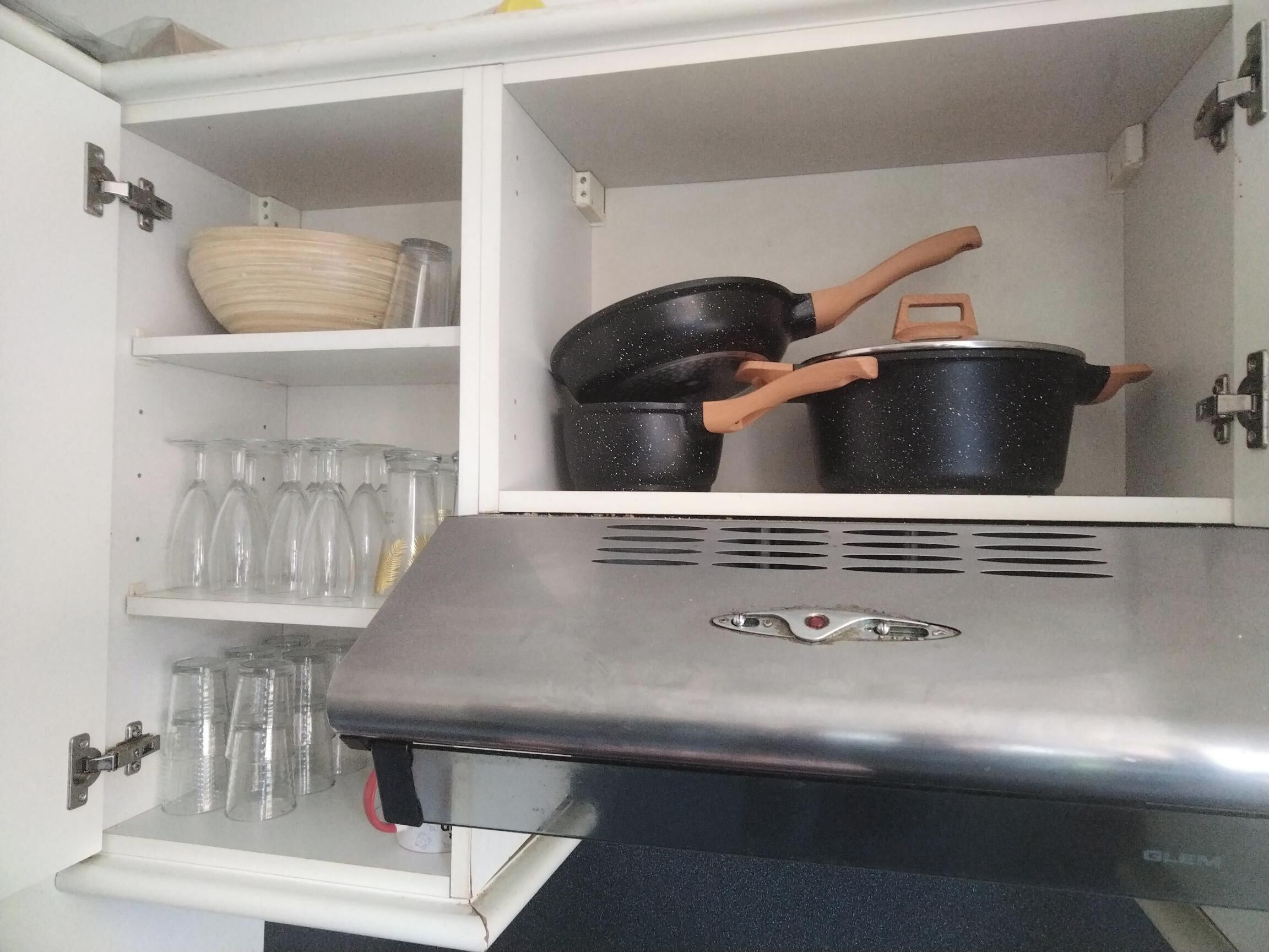 Una cocina con horno integrado, un estante con un tazón y una repisa con vasos.