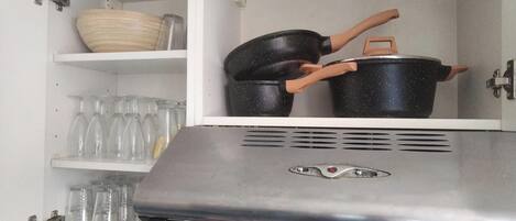 Una cocina con horno integrado, un estante con un tazón y una repisa con vasos.