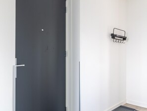 Una habitación con una puerta gris oscuro, una pared blanca y un estante negro fijado a la pared con ganchos.