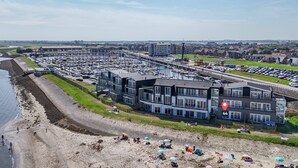 Un puerto deportivo con barcos, una playa con gente y un edificio moderno con balcones.