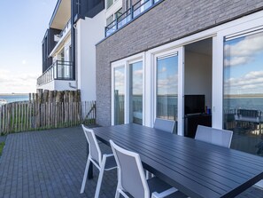 Un área de comedor al aire libre y moderna con una mesa larga, sillas, una valla de madera y vista al mar.