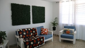 A living room with a white sofa, a blue armchair, and a coffee table. There are two green wall decorations and a potted plant. - Marina House  (Arroyo)