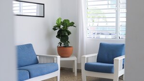 A room with two blue chairs, a white radiator, a potted plant, and a window with blinds. - Marina House  (Arroyo)
