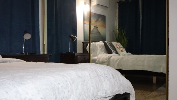 A bedroom with a large bed, a bedside table, a lamp, a mirror, and a painting on the wall. - Marina House  (Arroyo)