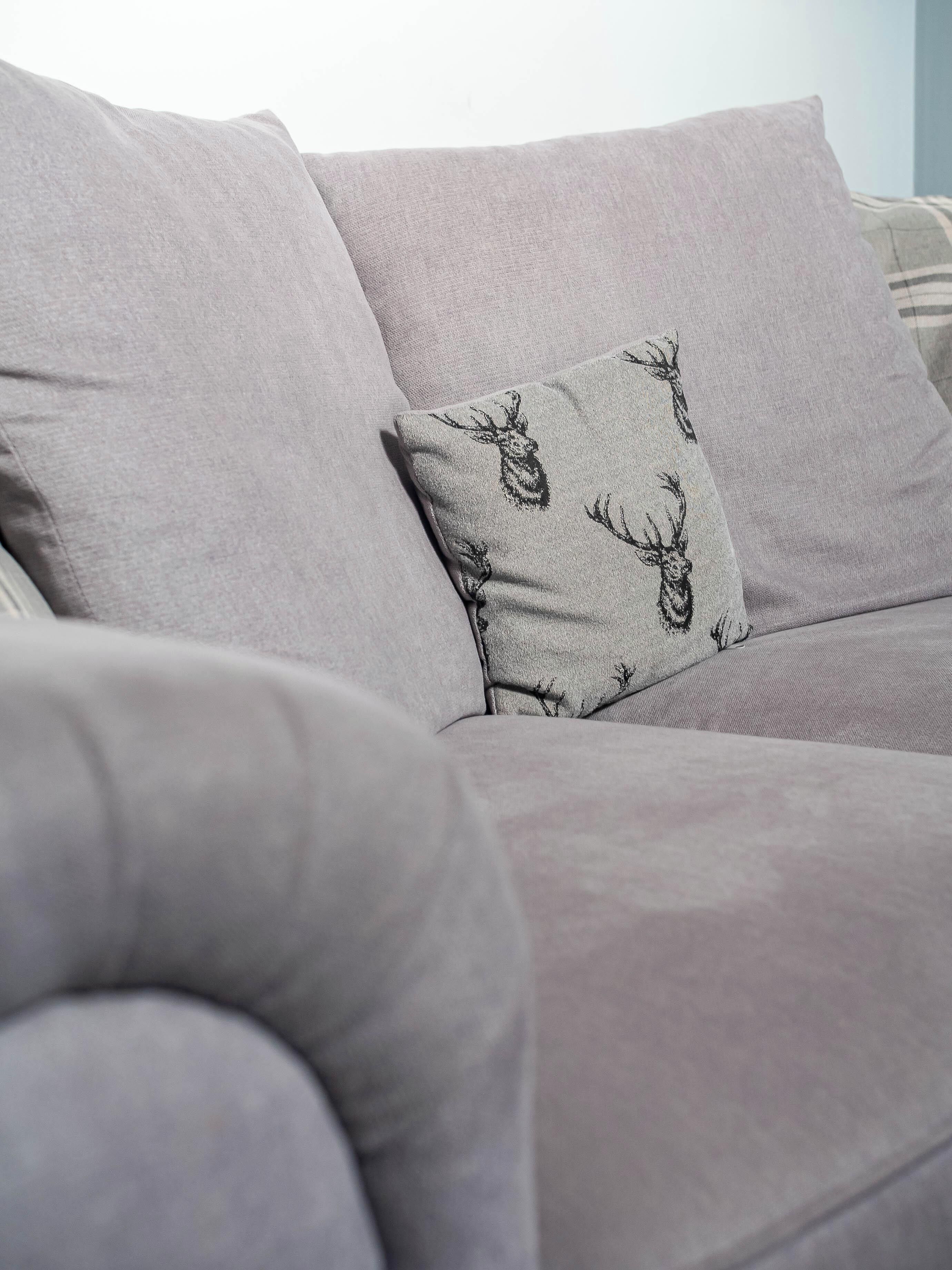 A grey sofa with a patterned pillow featuring deer designs.