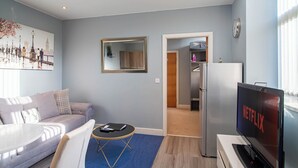 Un salon moderne comprenant un canapé, une table basse, un téléviseur et une porte donnant sur la cuisine.