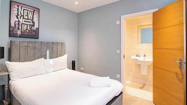 Une chambre d’hôtel moderne avec un grand lit, une table de chevet, une commode, un tableau accroché au mur et une armoire en bois.