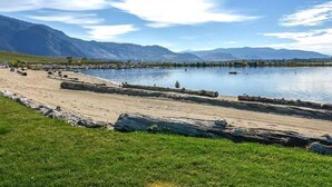 A lakeside view with a sandy beach, large rocks, and mountains in the background. - Mimi`s Cottage - Golf Cart Included (Osoyoos)
