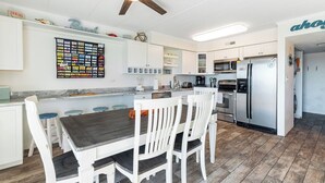 Una cocina moderna con armarios blancos, una isla central con taburetes de bar, un ventilador de techo y un refrigerador.