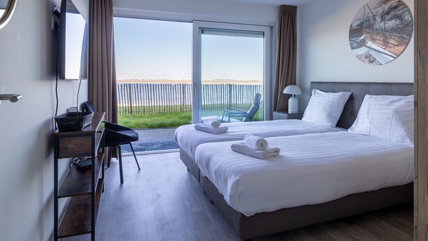 Habitación de hotel con una cama grande, un escritorio con silla, televisión y vista al mar.