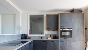 Una cocina moderna con horno empotrado, un lavabo y una zona de comedor con mesa y sillas de madera.