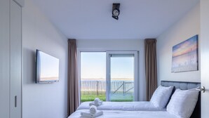 Un cuarto de hotel con dos camas, un ventanal con vista al mar, un cuadro en la pared y un reloj en el techo.