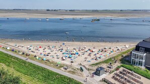 Una playa con tiendas de campaña y gente, una orilla arenosa y barcos en el agua.