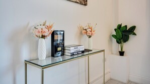 Ein Tisch mit Glasplatte, eine weiße Vase, eine schwarze Kaffeemaschine und Bücherstapel mit den Titeln 'Paris', 'London' und 'New York'.