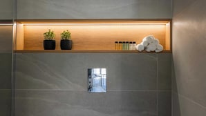 Et badeværelse med en træhylde med planter og toiletartikler, et spejl og udsigt til en gang.