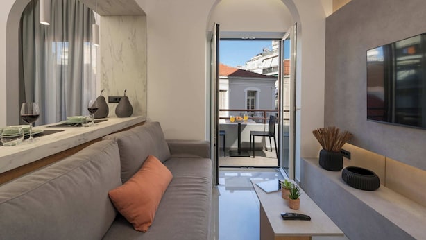 En moderne stue med sofa, sofabord og fjernsyn. Der er en balkon med bord og stole, synlig gennem en åben dør.