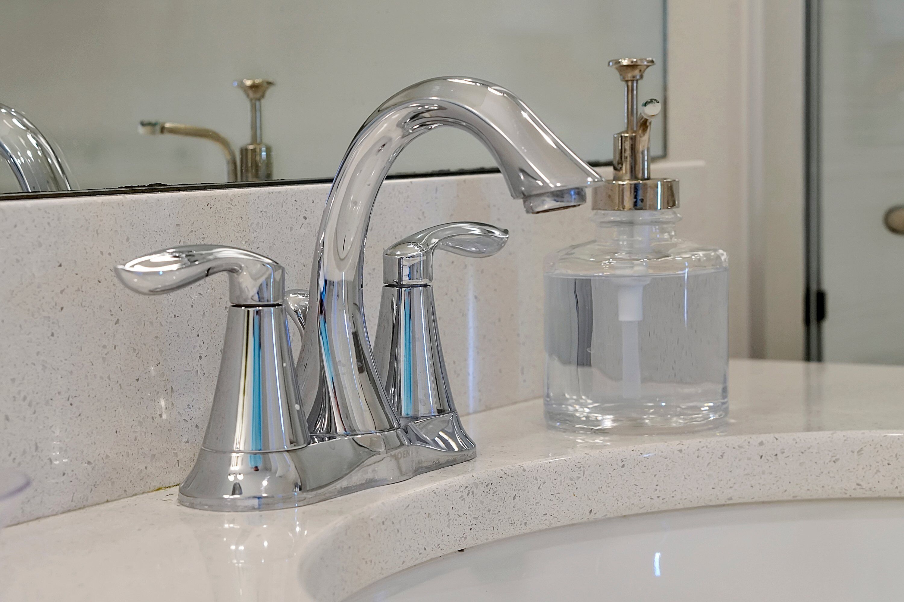 A bathroom with a chrome faucet and a clear glass soap dispenser on the sink.