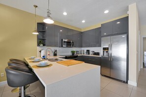 Una cocina moderna con gabinetes grises, un refrigerador de acero inoxidable, un microondas y una zona de bar con taburetes.