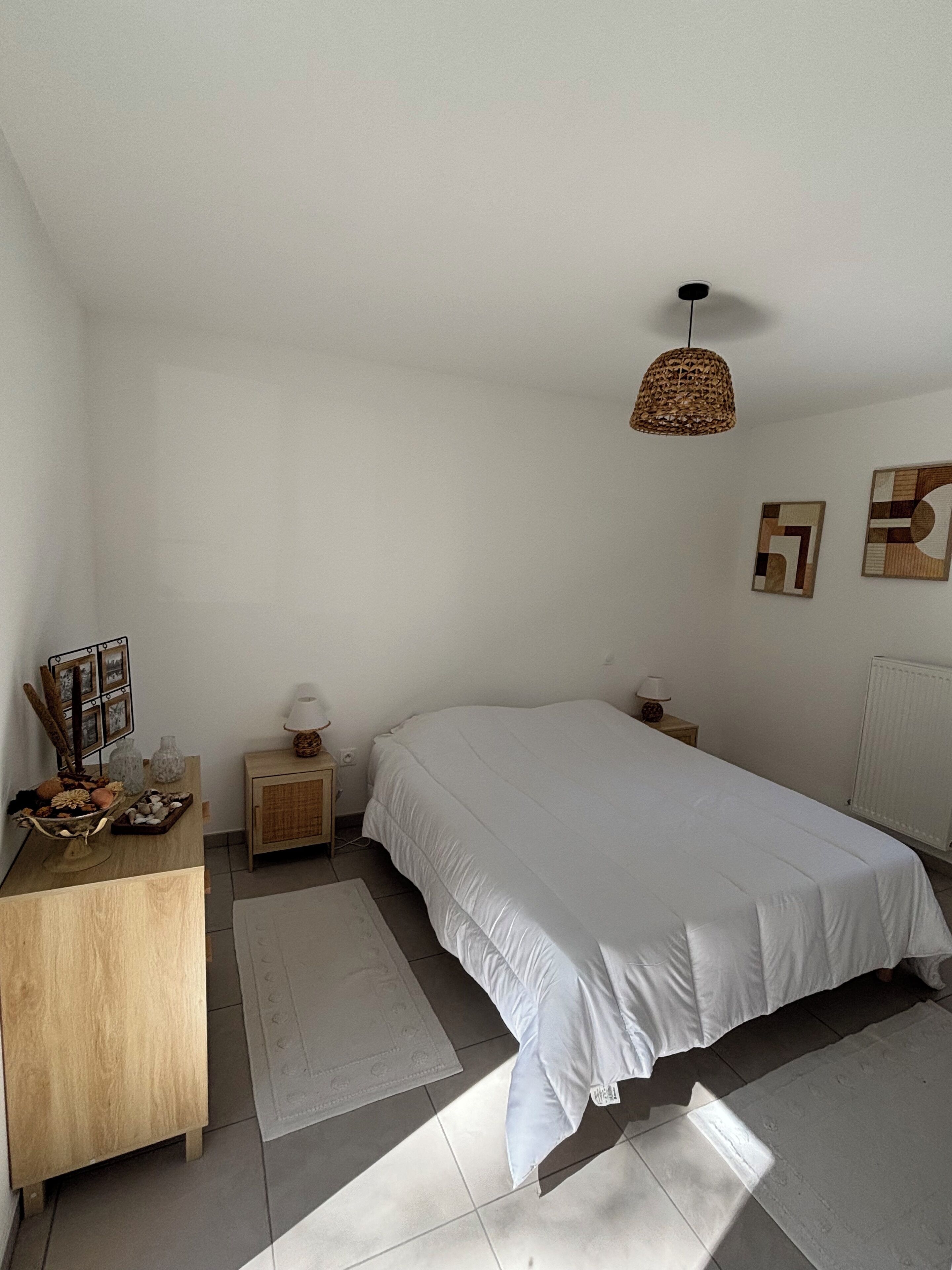 A bedroom with a large bed, a bedside table, a lamp, and a hanging light fixture.