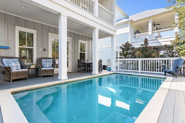 A poolside area with a covered patio, wicker furniture, and a white fence.