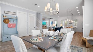 Une salle à manger spacieuse avec une longue table dressée pour six personnes, des chaises blanches et un lustre.
