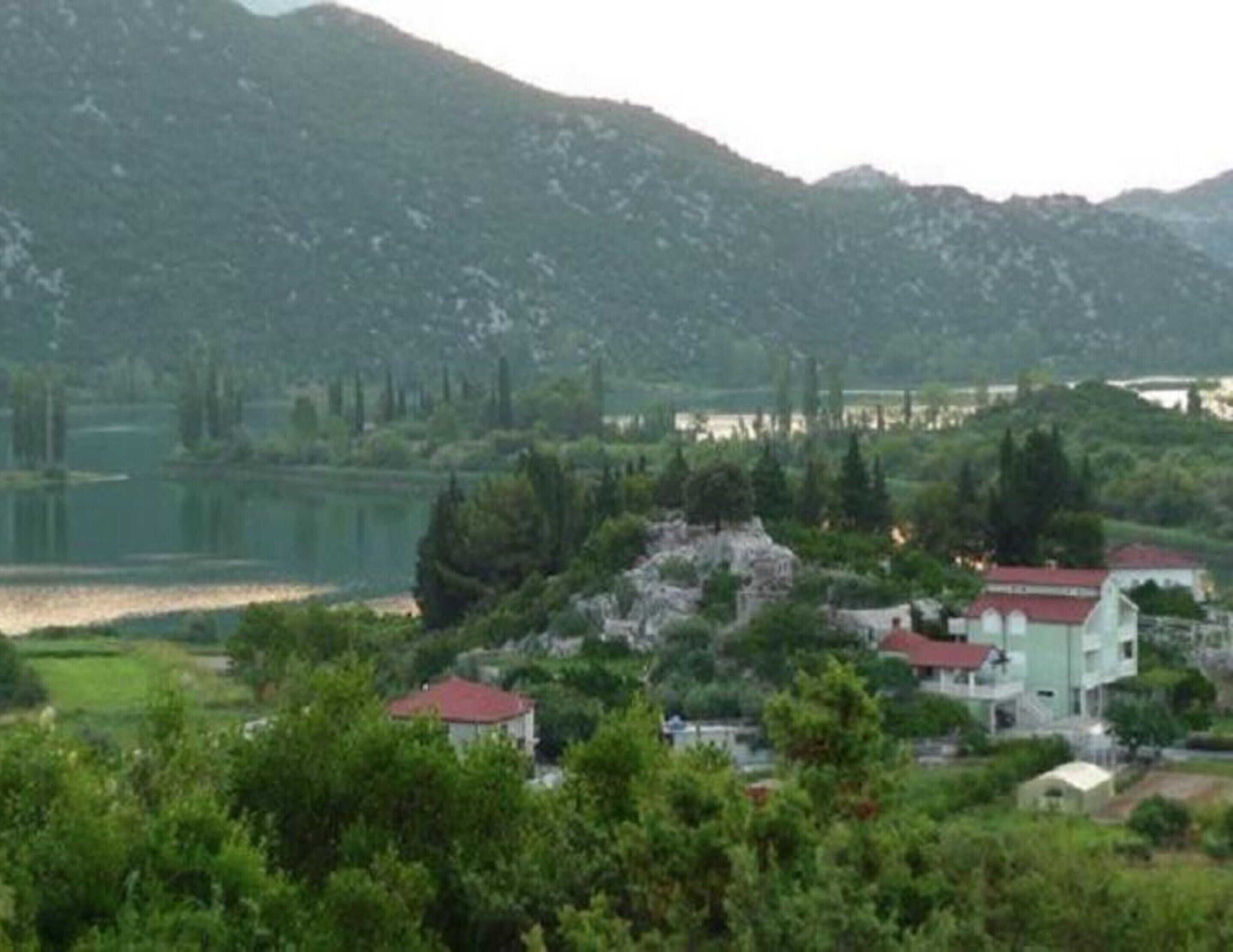 Un village au bord d’un lac, avec des bâtiments entourés de verdure et de collines.