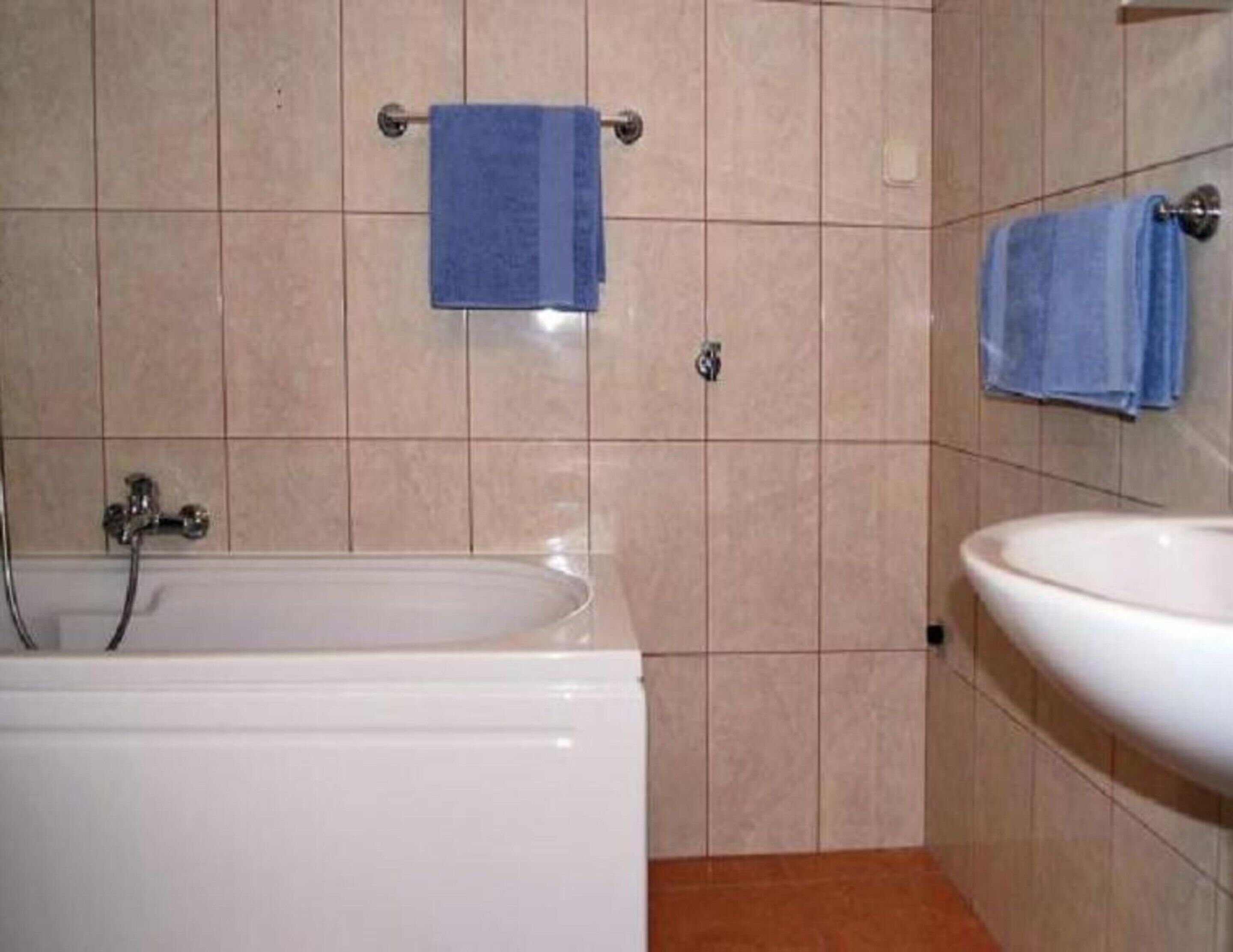 A bathroom with a bathtub, a sink, and two towels hanging on towel bars.