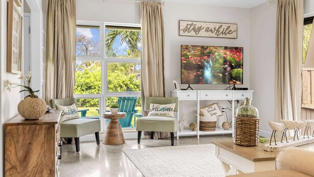 A living room with a TV, a sofa, a coffee table, and a view of greenery outside. - 3BR Cocoa Beach Oasis | 1 Block to Beach (Cocoa Beach)