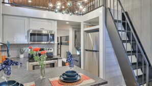 A modern kitchen with stainless steel appliances, a dining area with a marble countertop, and a staircase leading to an upper level.