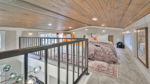 A bedroom with a wooden ceiling, a bed with a patterned blanket, a small rug, and a wall-mounted fan.