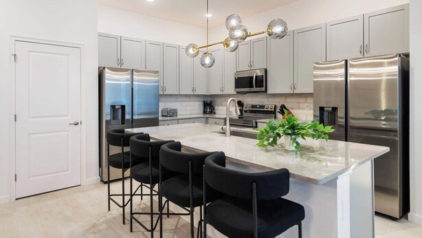 A modern kitchen with stainless steel appliances, a central island with bar stools, and a decorative light fixture.