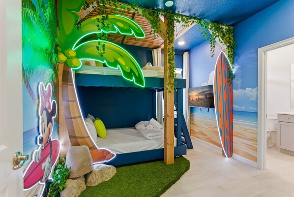A room with a bunk bed, artificial palm trees, a surfboard mural, and a Mickey Mouse cutout.