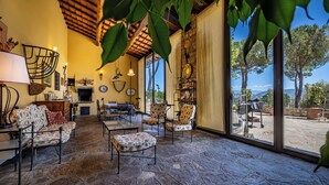 A cozy interior with stone flooring, a fireplace, and a view of trees through large windows. - Villa Dei Pavoni - Luxury Villa on top of hills in Florence (Toscana)