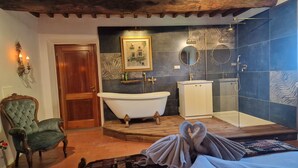 A room with a bathtub, a shower, a wooden chair, and a bed with towels. - Villa Dei Pavoni - Luxury Villa on top of hills in Florence (Toscana)