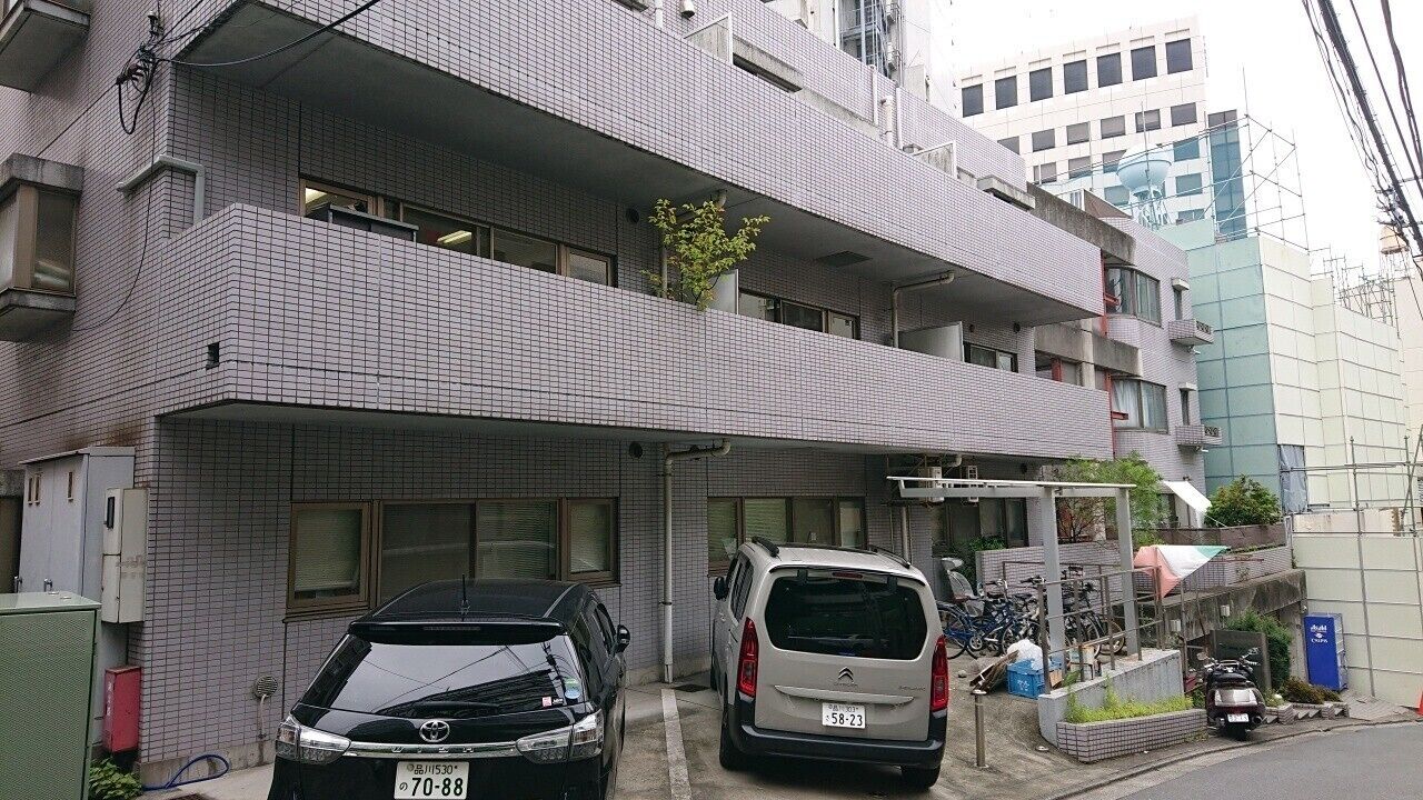 A multi-story residential building with a tiled facade, a balcony, and parked cars.