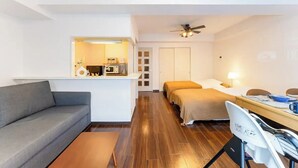 Ein kompaktes Hotelzimmer mit einer Schlafcouch, einem Bett, einem Schreibtisch mit Stuhl und einer Küchenzeile.