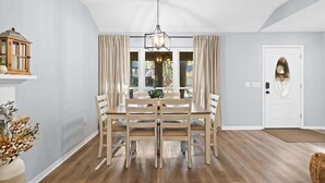 Un comedor con una mesa y sillas de madera, una lámpara colgante y una puerta blanca con un panel de vidrio decorativo.