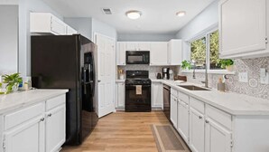 Una cocina moderna con armarios blancos, un refrigerador negro, un microondas y una estufa.