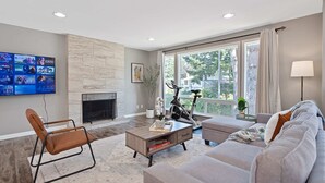 A modern living room with a fireplace, a mounted TV, a sofa, and a bike. - Chic Kirkland Home Overlooking Windsor Vista Park (Kirkland)