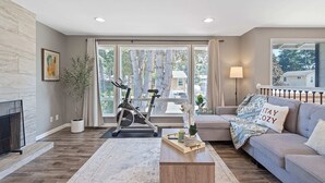 A living room with a fireplace, a sofa, a coffee table, and an exercise bike. - Chic Kirkland Home Overlooking Windsor Vista Park (Kirkland)