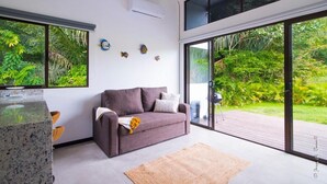 Una sala moderna con un sofá gris, una alfombra pequeña y un amplio ventanal corredero que da a una terraza de madera.