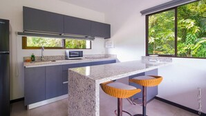 Una cocina moderna con armarios grises, encimera de granito, microondas y dos taburetes de mimbre.