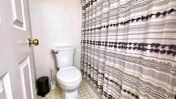 Un bagno con il water, un cestino nero e una tenda da doccia fantasia.