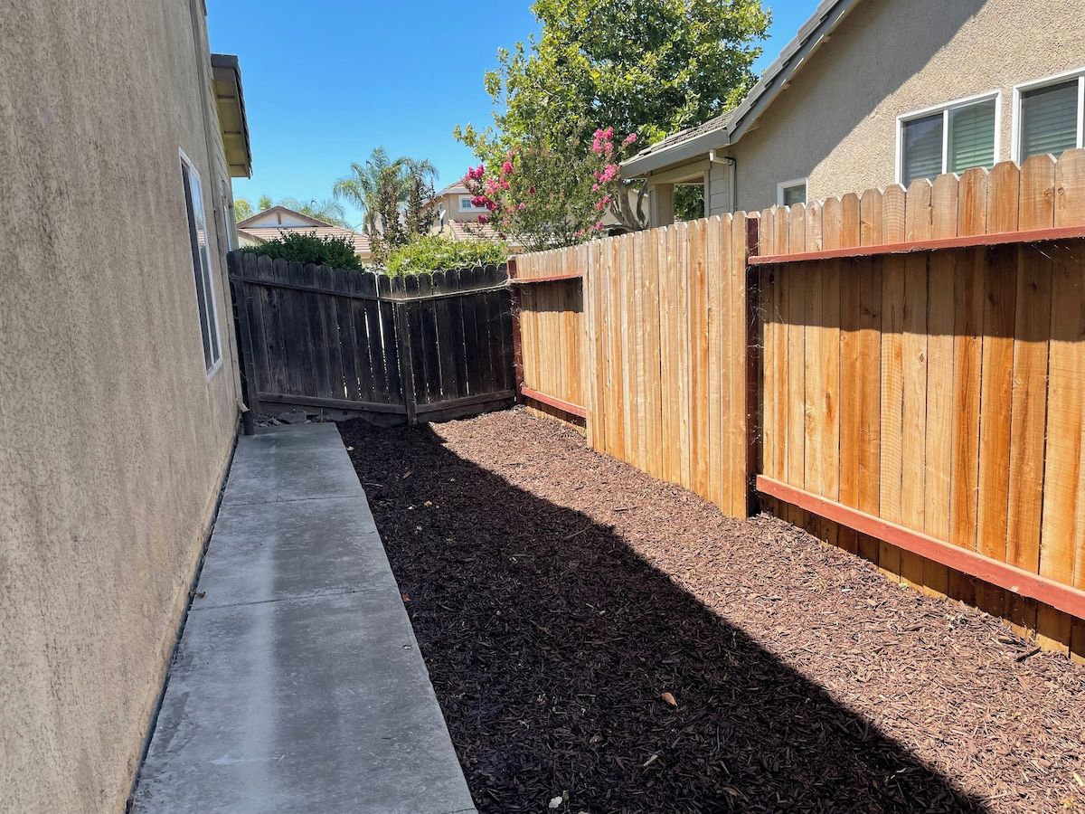 Ein Garten mit einem Betonweg, einem Holzzaun und einer Mulch-Bodenabdeckung.