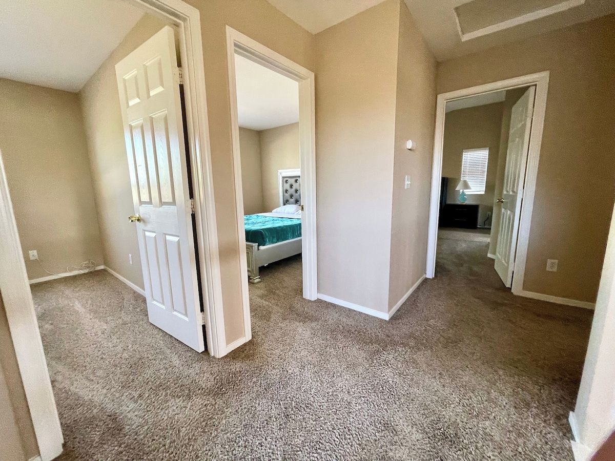 A hallway with carpeted floors and white walls, leading to a bedroom with a bed and a nightstand.