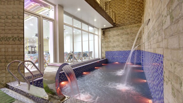 A spa area with a hot tub, glass doors, and a view of the outside. - MIYABI HOTEL (Gurugram)