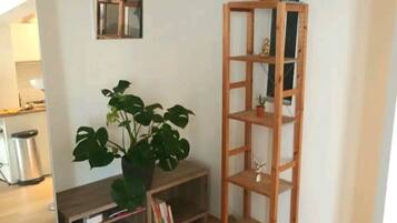 A corner room with a wooden floor, a bookshelf, a potted plant, and a small table.
