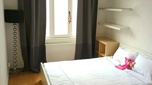 Une chambre à coucher avec un lit, une table de chevet, une lampe et une fenêtre avec des rideaux.