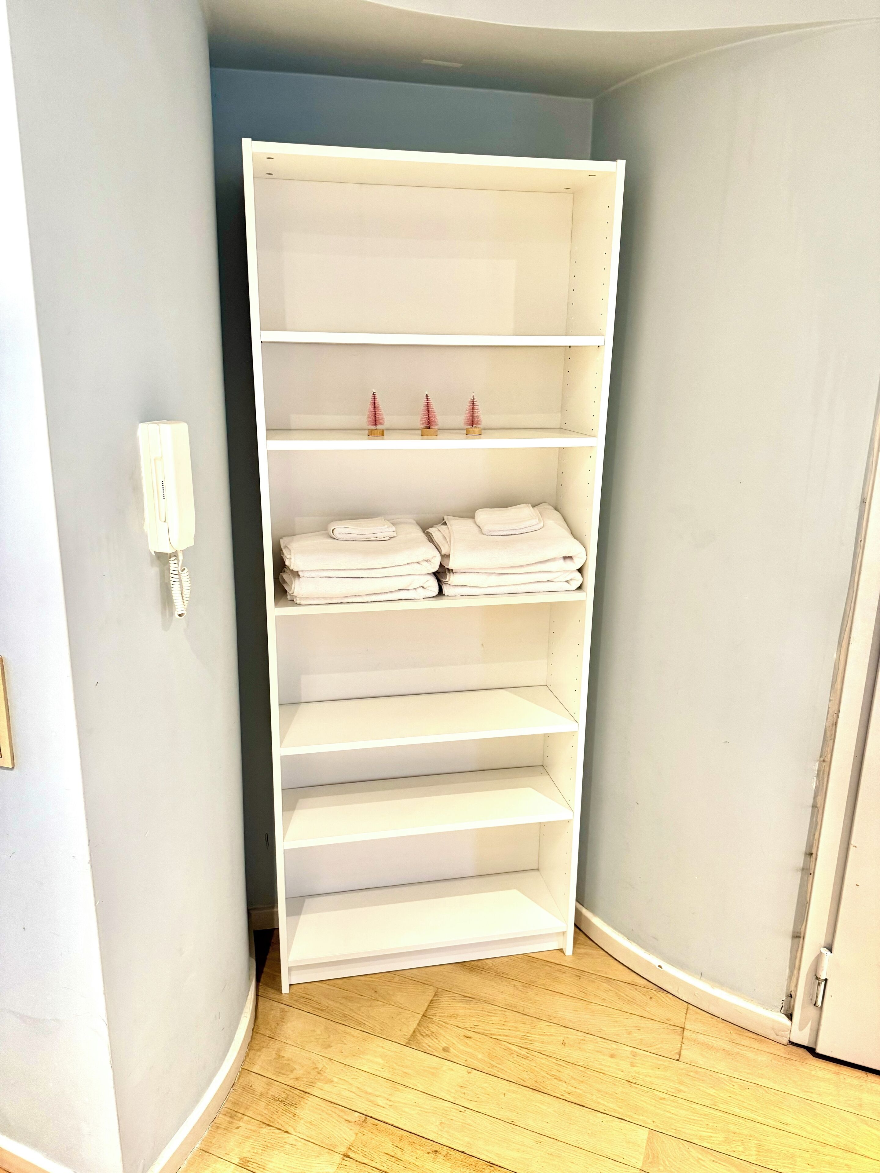 A corner room with a white shelving unit, a white telephone, and a wooden floor.